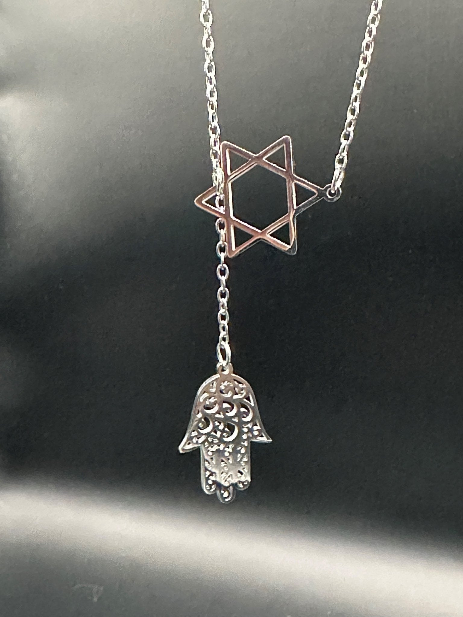 Star of David and Hamsa Drop Necklace - Simply Just Deals LLCStar of David and Hamsa Drop NecklaceJewelry Pendant Necklace42560115703831GoldThe Star of David and Hamsa Drop Necklace showcases a silver open star with a decorative Hamsa hand charm suspended below, displayed on a plain black background.