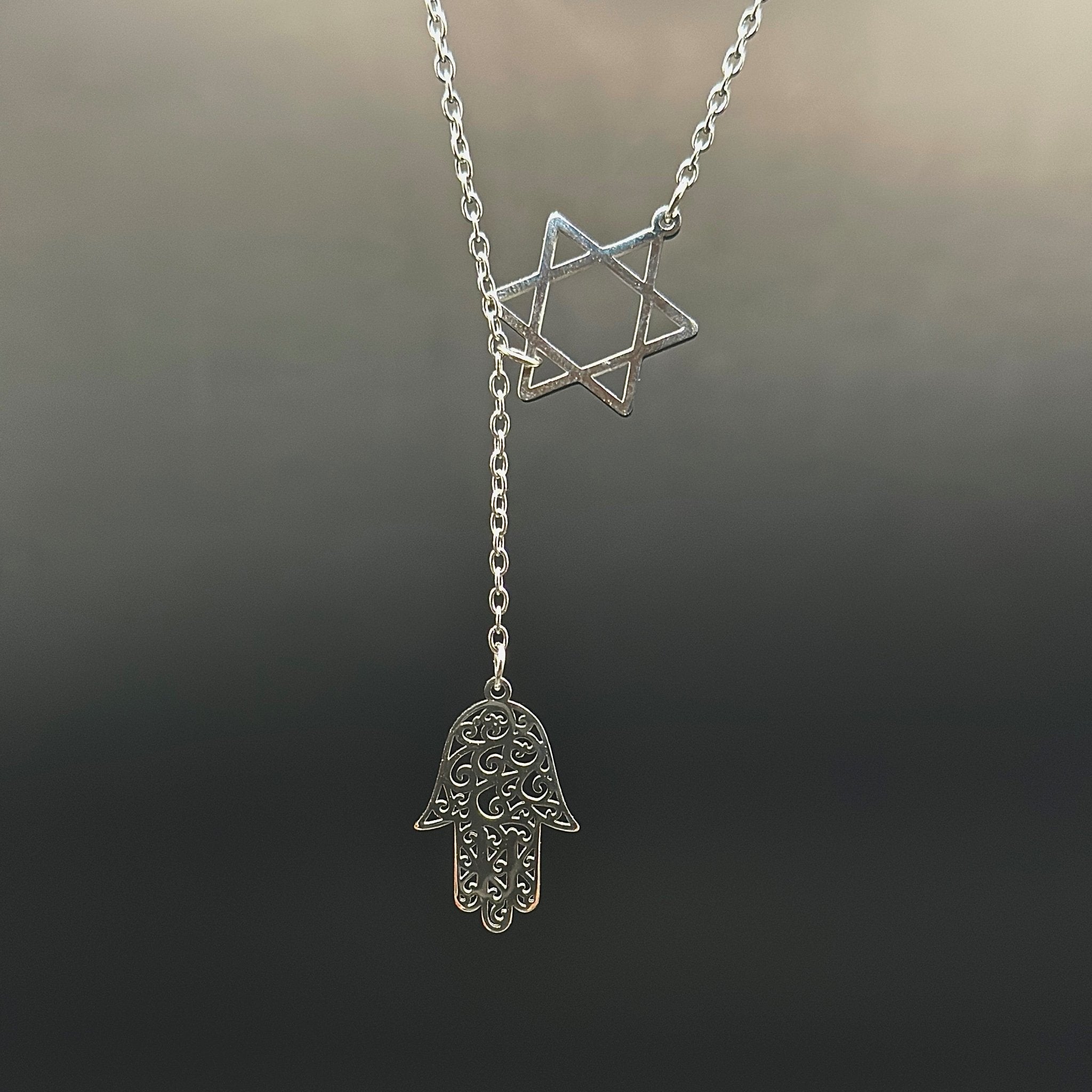 Star of David and Hamsa Drop Necklace - Simply Just Deals LLCStar of David and Hamsa Drop NecklaceJewelry Pendant Necklace42560115703831GoldThe Star of David and Hamsa Drop Necklace features a silver Star of David and an ornate Hamsa hand charm on a delicate chain, both gleaming softly against a dark, blurred background.